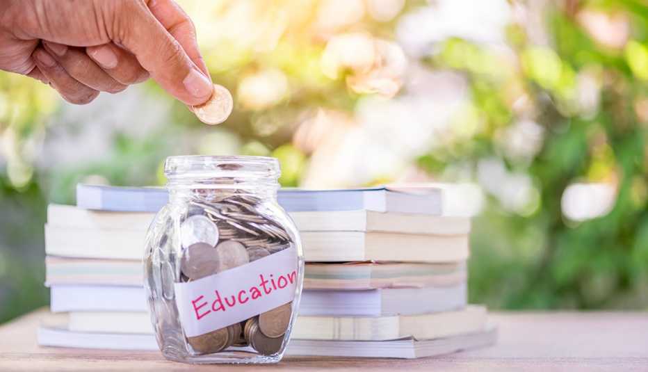 Mano colocando una moneda en una jarra con el letrero educación