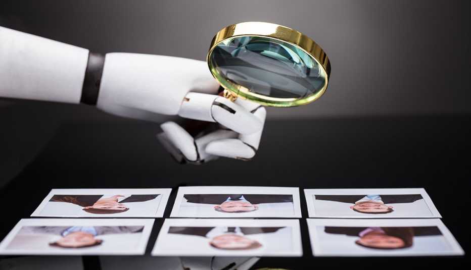 Mano de un robot sosteniendo una lupa sobre varios retratos