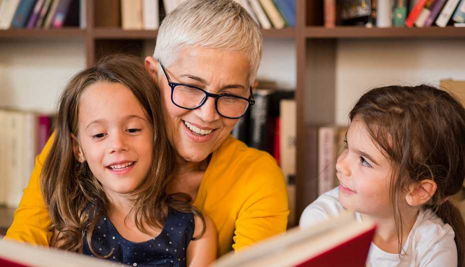 Mujer mayor leyendo un libro a dos niñas.