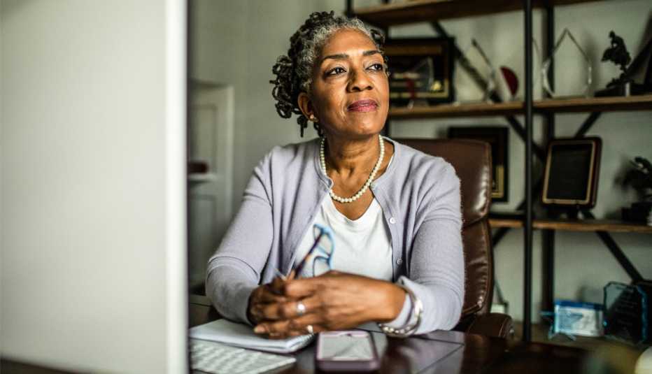 Mujer mayor en la sala de su casa frente a una computadora y mirando hacia un lado