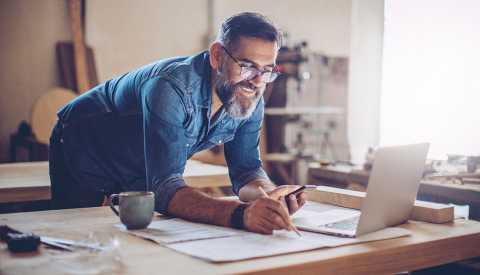 Carpintero en su taller dibujando un plano al lado de su computadora