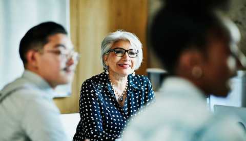 Mujer mayor sentada en una oficina con dos personas más.