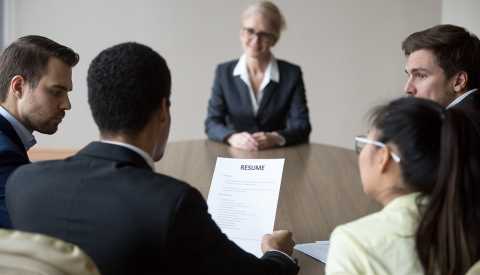 Grupo de personas en un sala de juntas que entrevista a una mujer mayor.