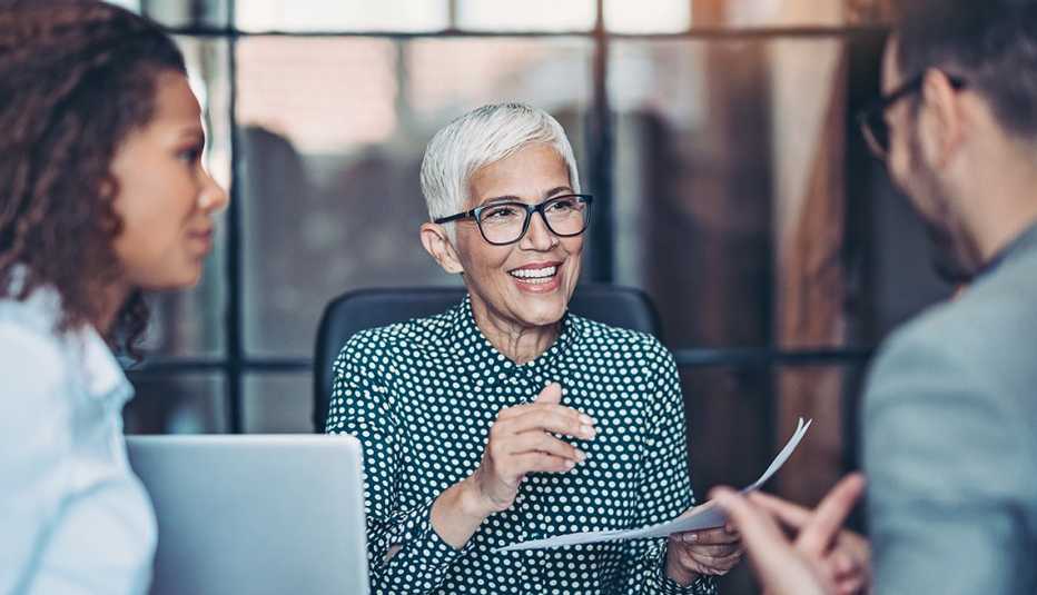 Mujer mayor hablando en una oficina con una mujer y un hombre.