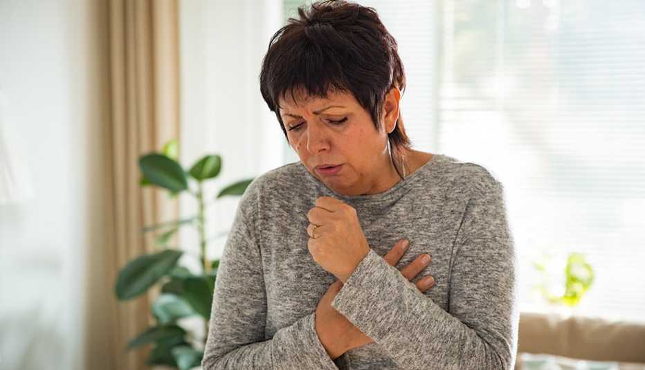 Mujer tosiendo y con los brazos en el pecho.