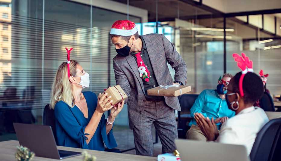 Empleados en una oficina en una fiesta de navidad con gorros navideños y mascarillas