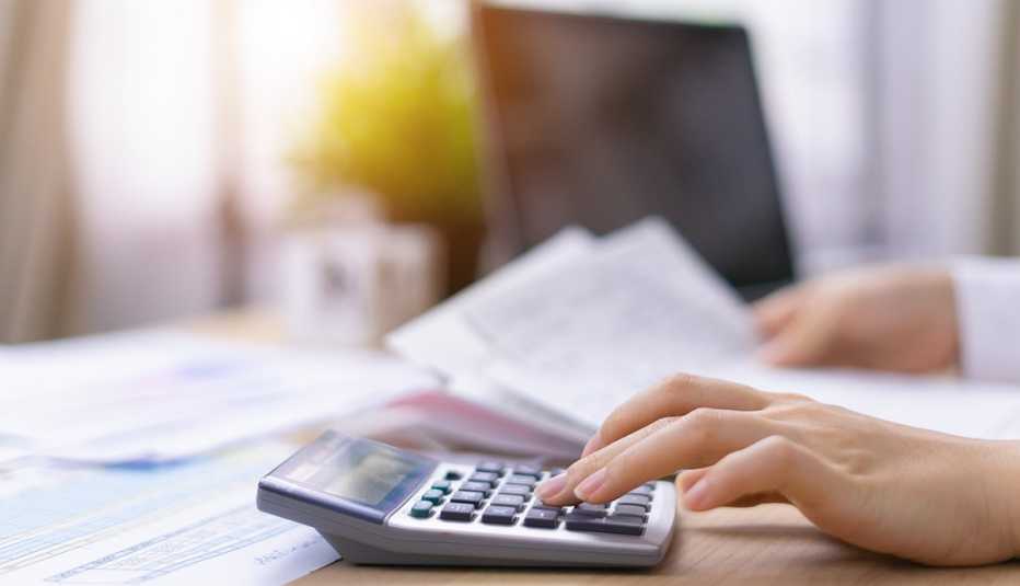 Mano de una persona que hace cuentas en una calculadora y con la otra sostiene unas facturas. 