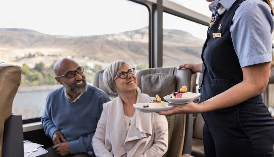 Camarera ofrece postre a un hombre y una mujer en el tren Rocky Mountaineer