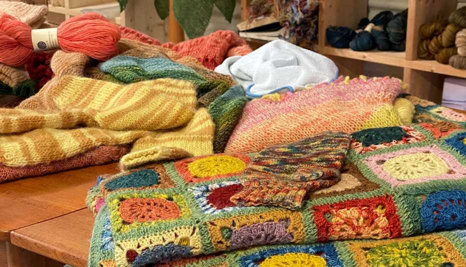 Madejas de hilo, una manta cuadrada multicolor y un suéter a rayas Madejas de hilo, una manta cuadrada multicolor y un suéter a rayas