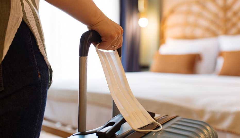 Mujer con mascarilla quirúrgica llega con una maleta a una habitación del hotel