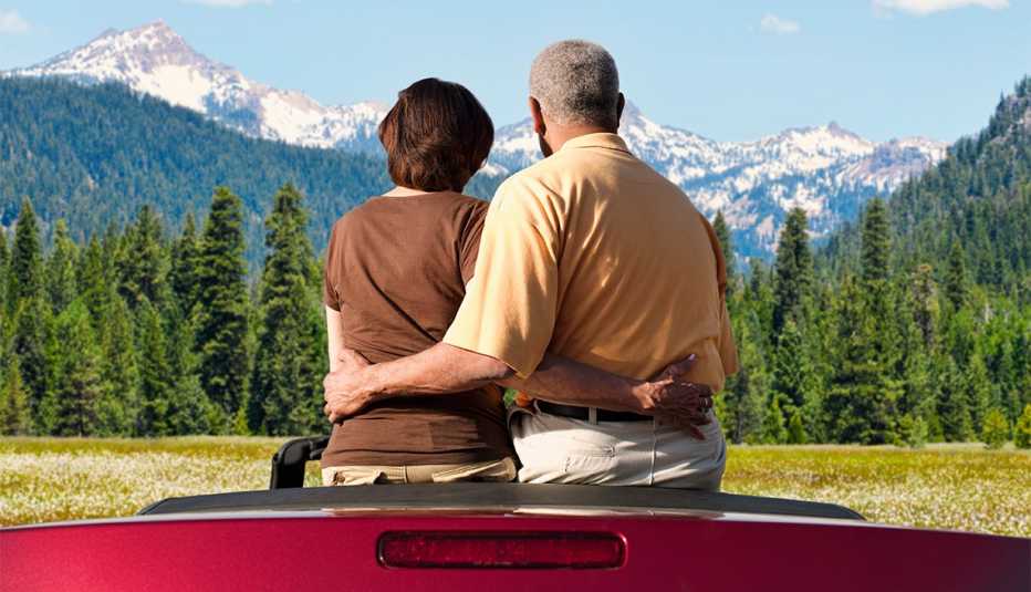 Pareja sentada en un auto convertible mira las montañas