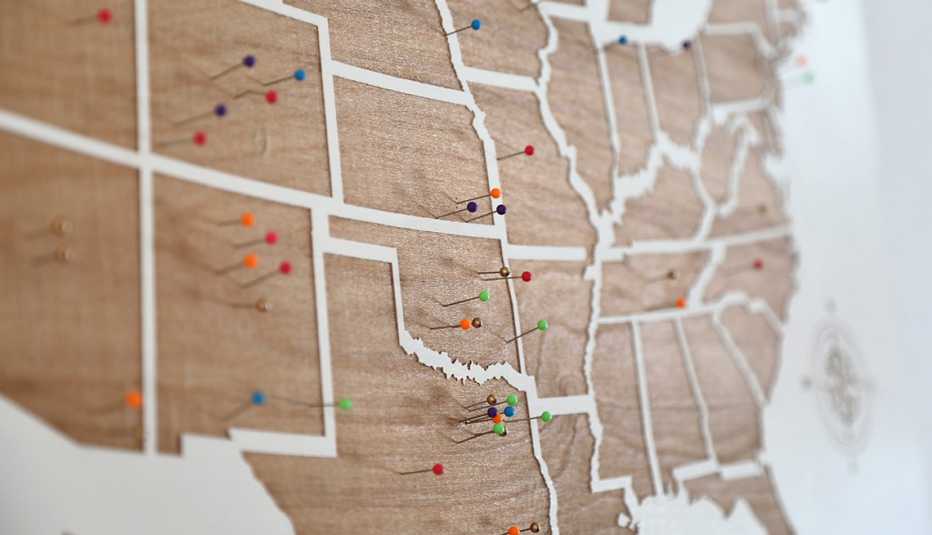 Wooden US States map on the wall with multicolored pins on it.