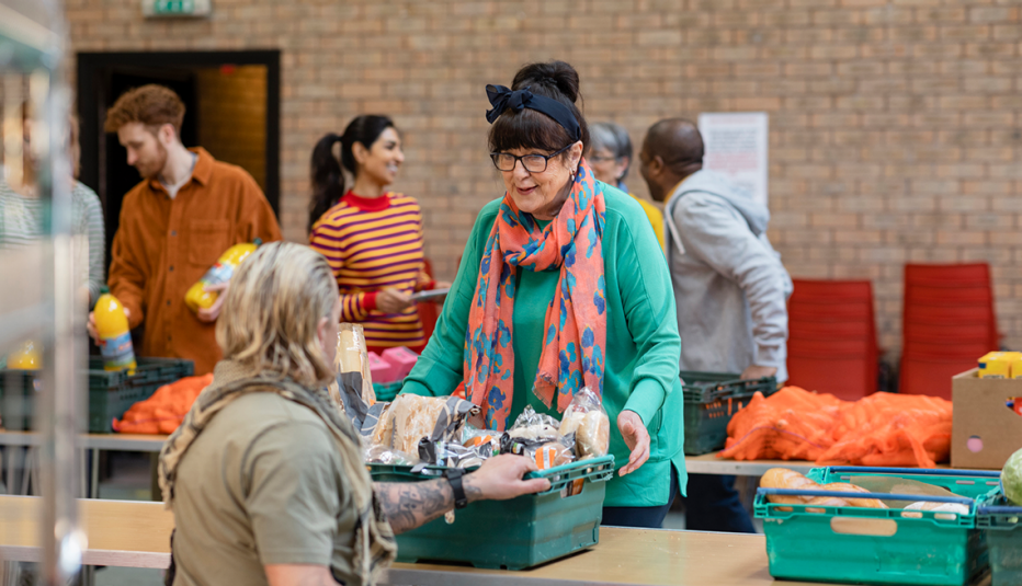 Woman working in a food pantry with others giving a basket of food to someone in need