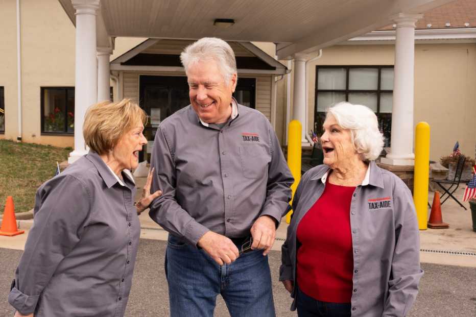 Sisters Charlotte (left) and Carolyn flank Carolyn’s husband, Jeff – outside the senior center where all three volunteer for Tax-Aide.
