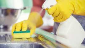 Persona limpia el fregadero de la cocina con una esponja y una botella de spray Persona limpia el fregadero de la cocina con una esponja y una botella de spray