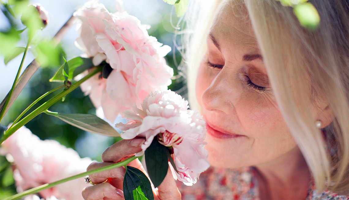 Mujer huele de cerca unas flores de color rosado