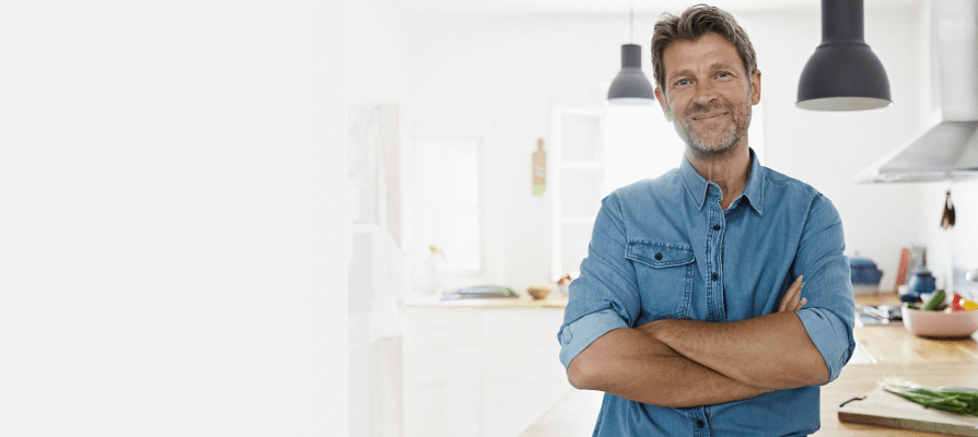 man with folded arms wearing jean shirt standing in bright kitchen