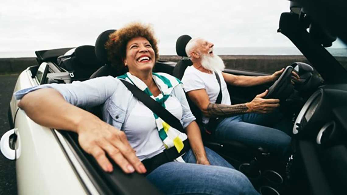 man driving and woman in passenger seat of convertible car smiling on cloudy day
