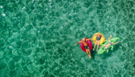 overhead look at two people sitting on tubes and one on a raft in water