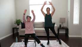 two women exercising in their living room with their arms raised