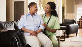 Woman in wheelchair talking with a female nurse inside a home