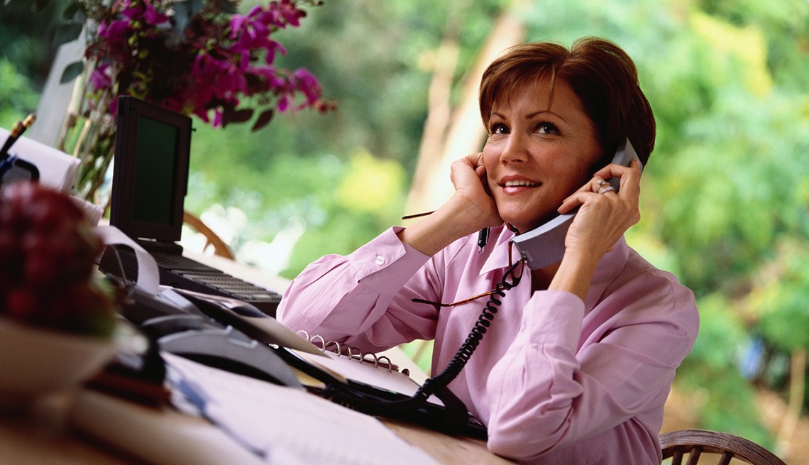 Mujer con blusa rosa hablando por teléfono en su escritorio