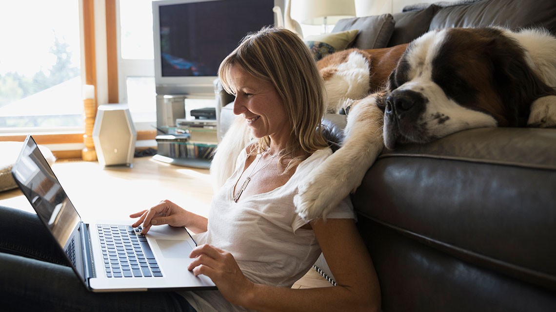 Una mujer sentada, junto a su perro, mira su computadora.