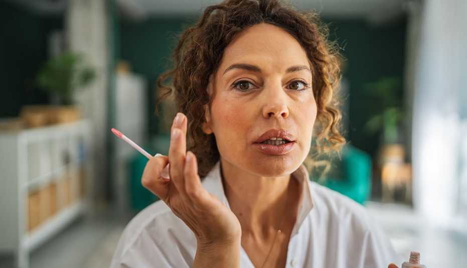 Woman holding a lip gloss applicator with puckered lips, looking directly at the camera while applying makeup during her daily beauty and skincare routine