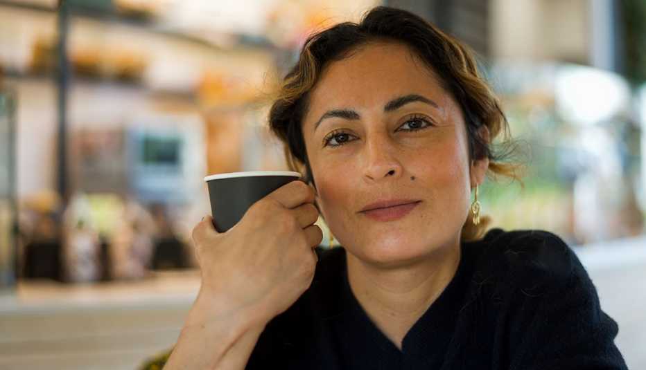 Older adult holding a coffee cup in a café setting.