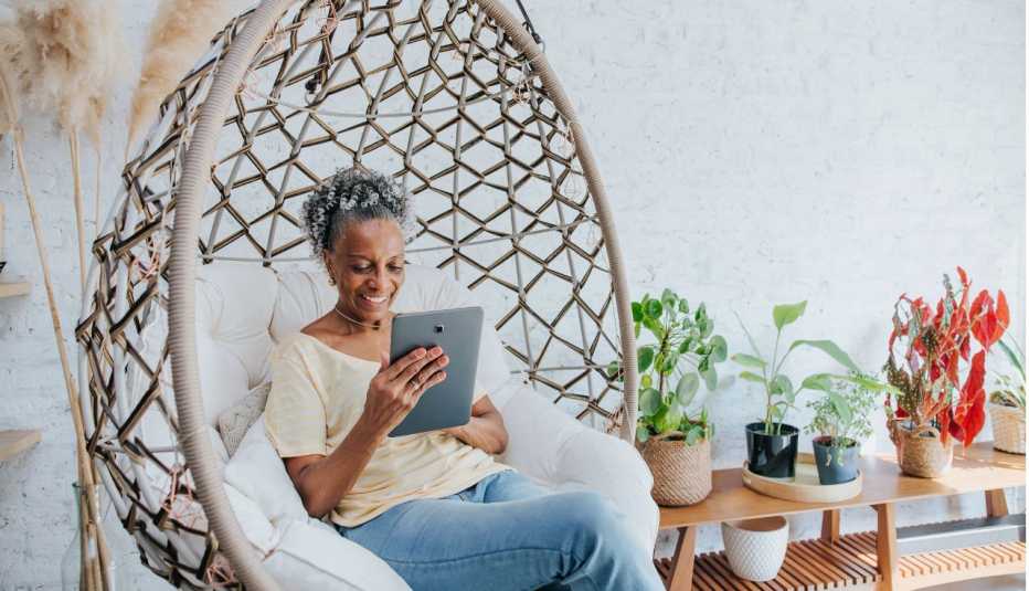 happy woman sitting in a swinging chair looking at her tablet