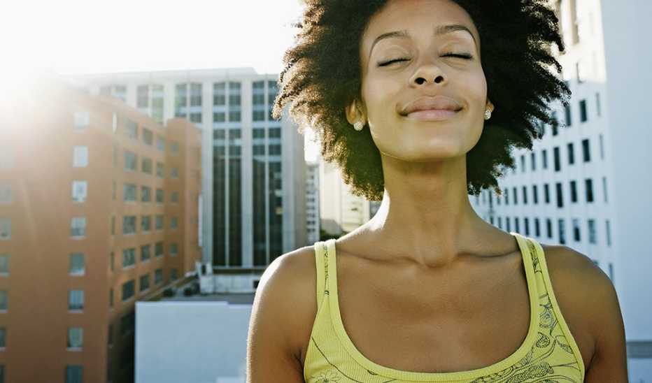 A woman with her eyes closed taking in the outdoors in a city