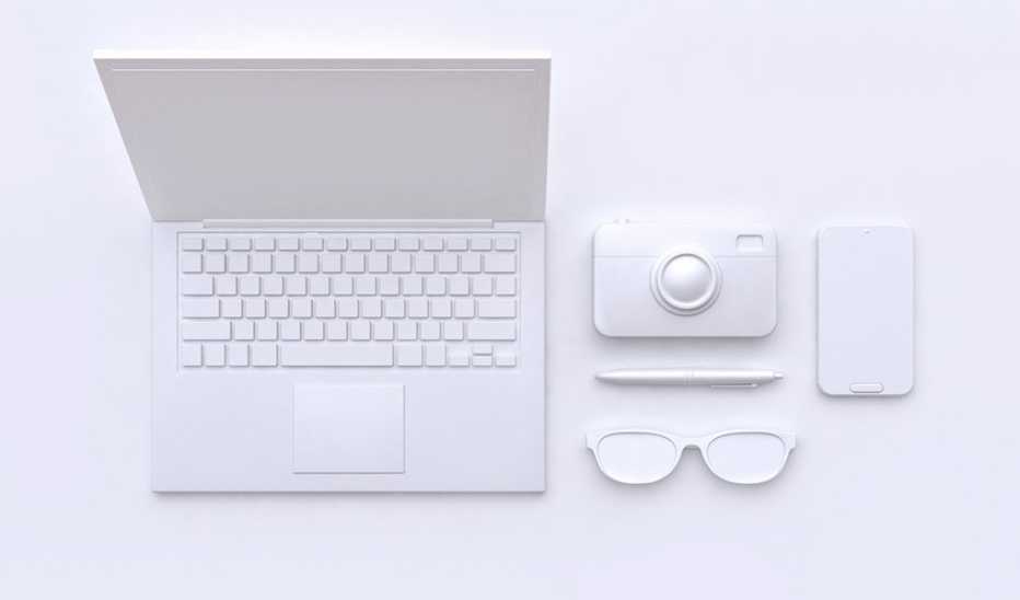 A plain white laptop, camera, smartphone, pen and glasses sitting on a white backdrop