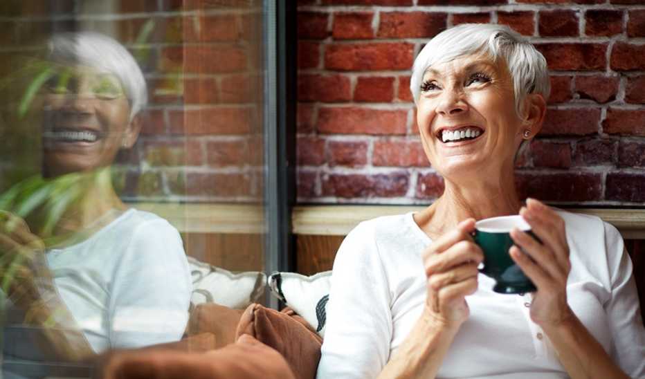 A woman smiling while drinking coffee by a window