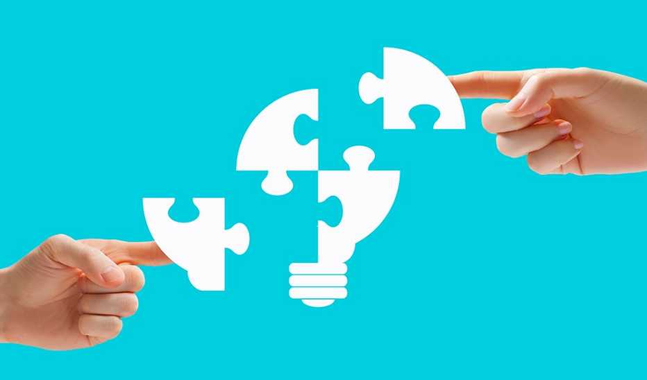 Two hands putting together four puzzle pieces to make a lightbulb image