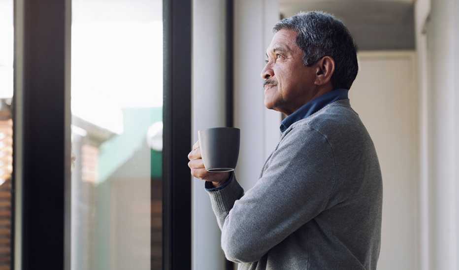 A man looking out a window with a coffee in his hand