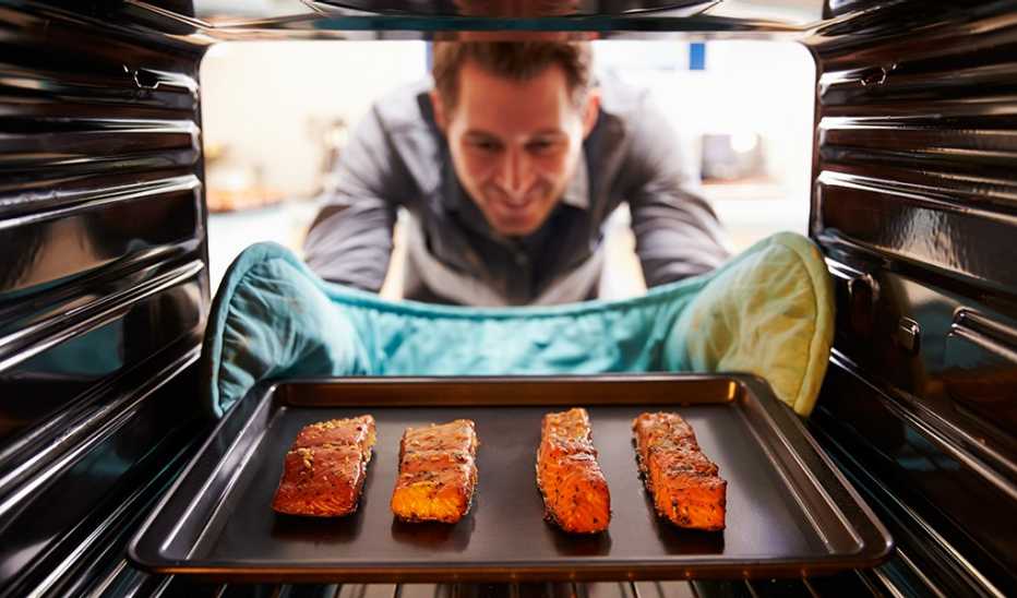A man taking a tray of salmon fillets out of the oven
