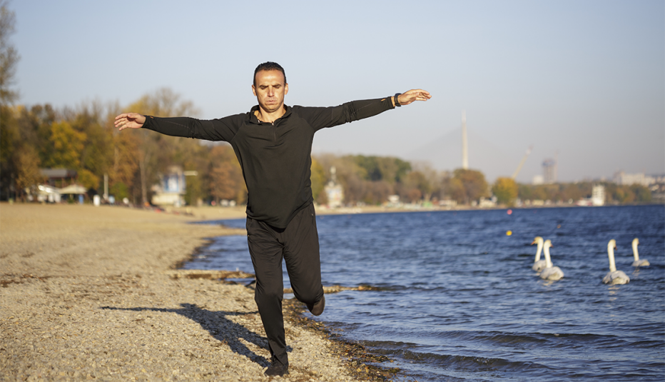 A man balancing on one leg on a beach