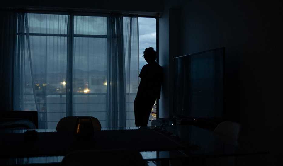 A silhouette of a man standing in the dark by a window at home