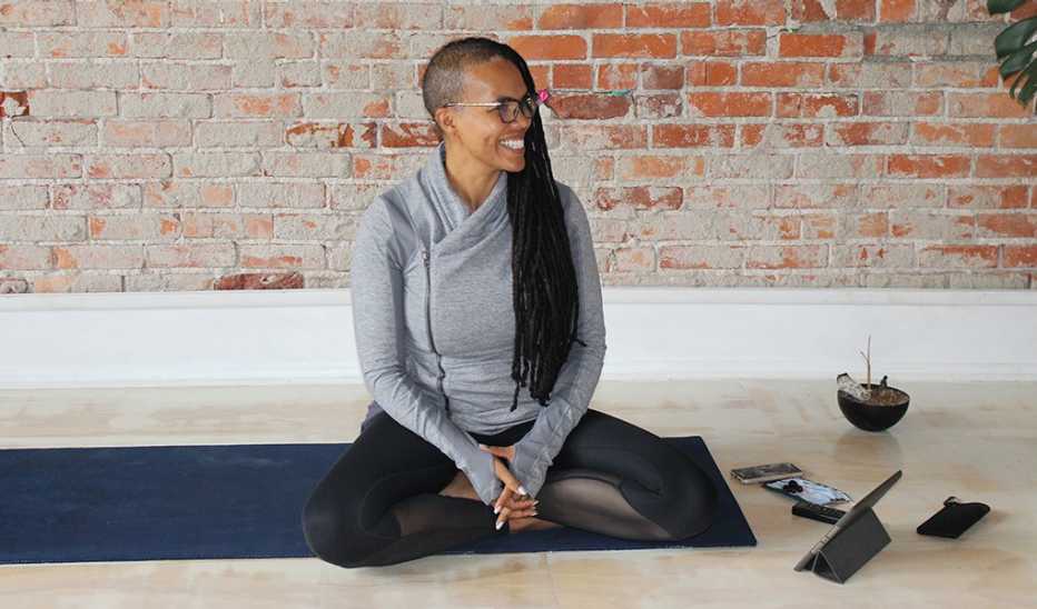 A woman, Ali Duncan, smiling and sitting on a mat in a yoga studio