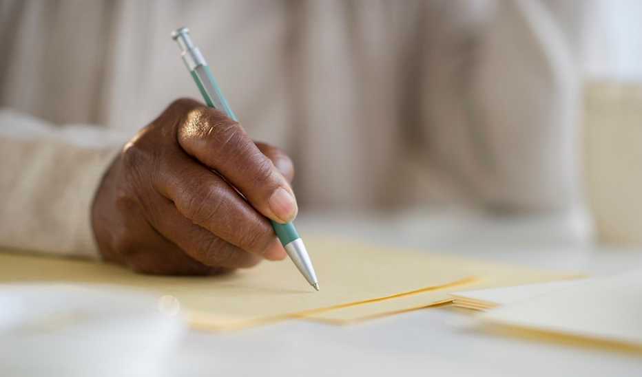 A close up of a hand writing with a pen on paper