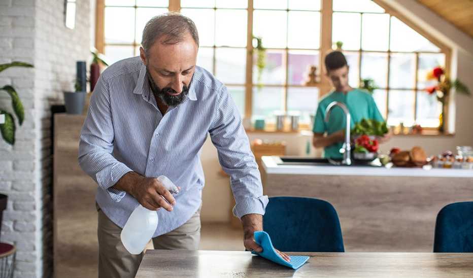 A man using a spray bottle and rag to clean a table