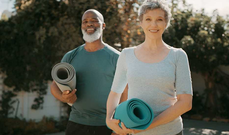A smiling man and woman holding yoga mats outside