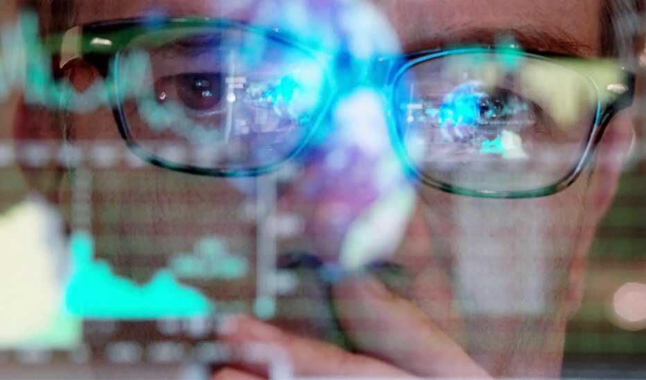 A close-up view of a man with glasses looking at a screen