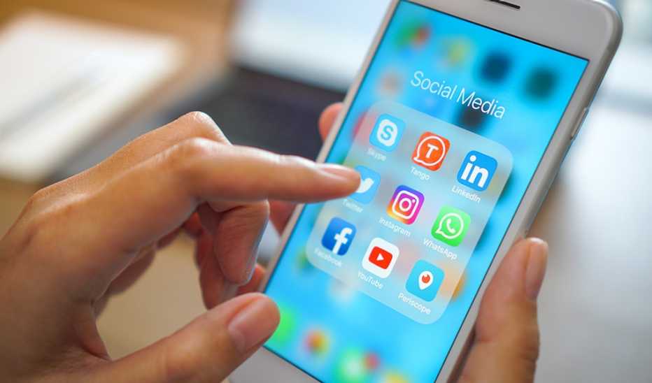 A hand looking to select one of several social media apps on their smartphone