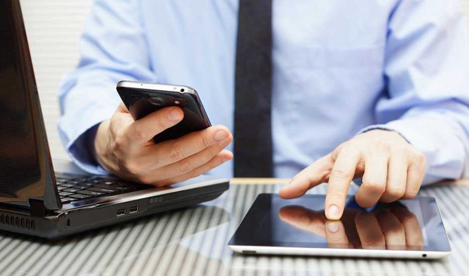 A businessman is working on a tablet and using a smartphone in an office