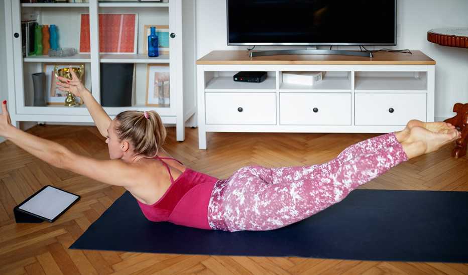 A woman doing the Superman exercise on a yoga mat inside a home