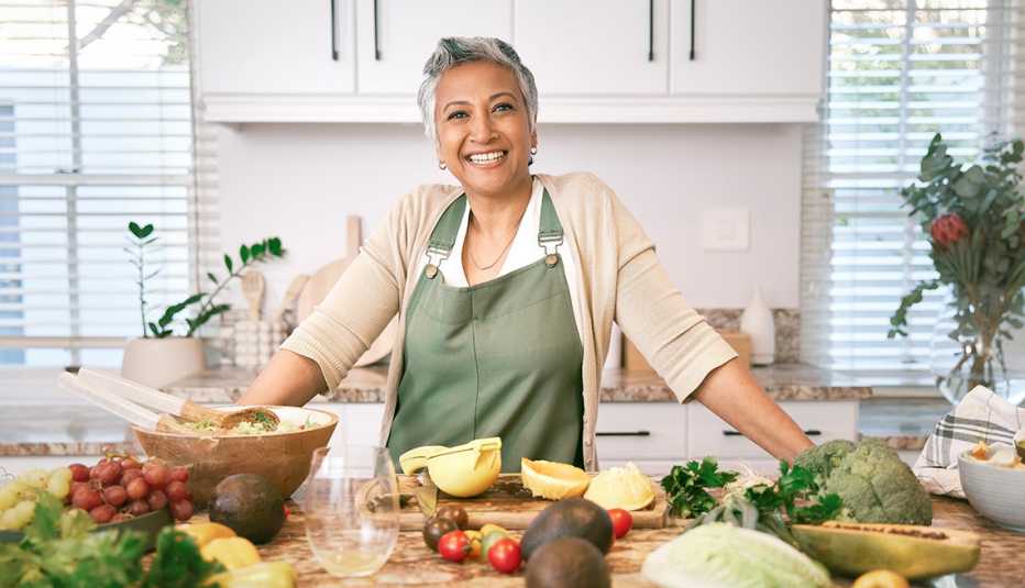 A smiling woman posing in front of a lot of vegetables in a kitchen