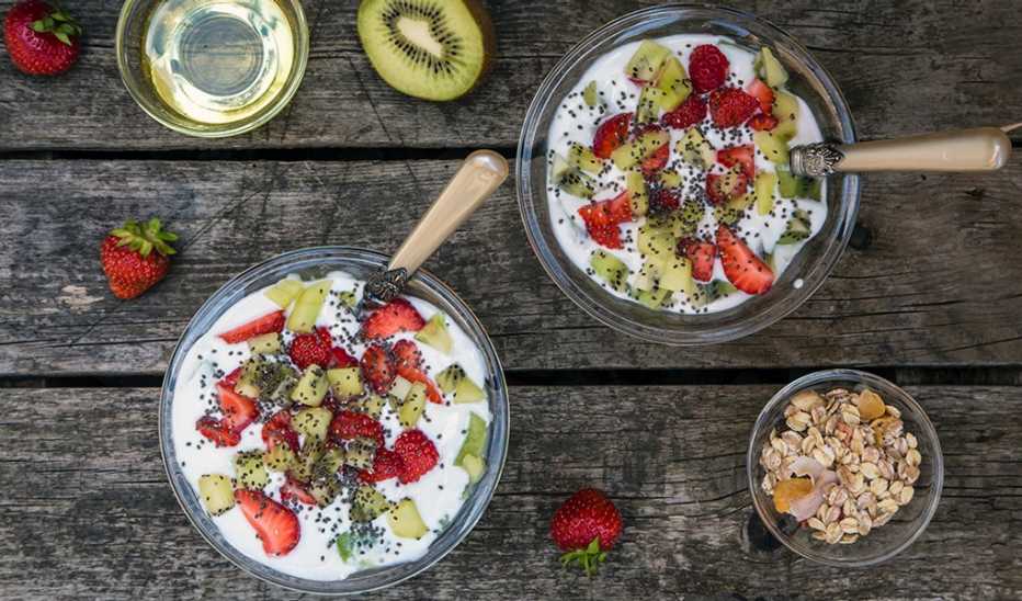 A strawberry kiwi yogurt with cereals, chia seeds and agave syrup in a glass bowl on wood