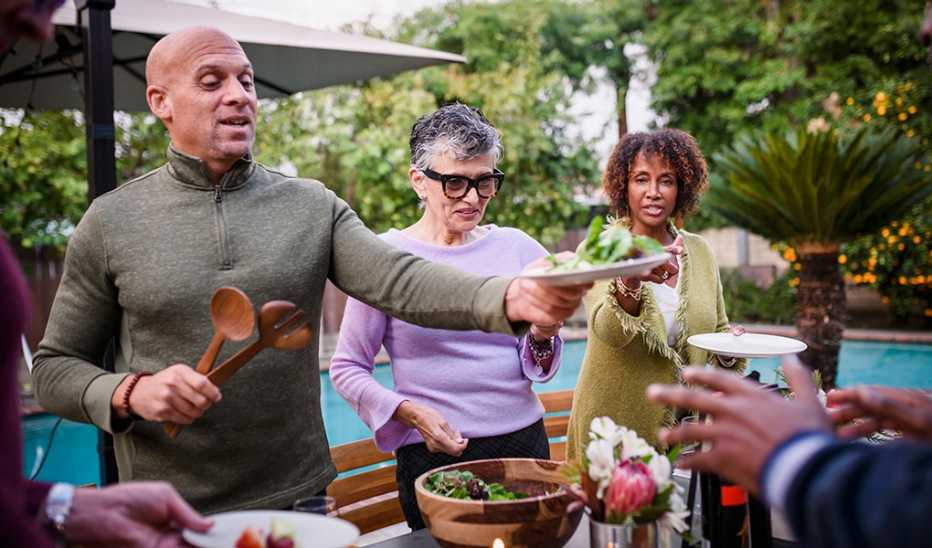 A man serving salad to people at an outdoor dinner party