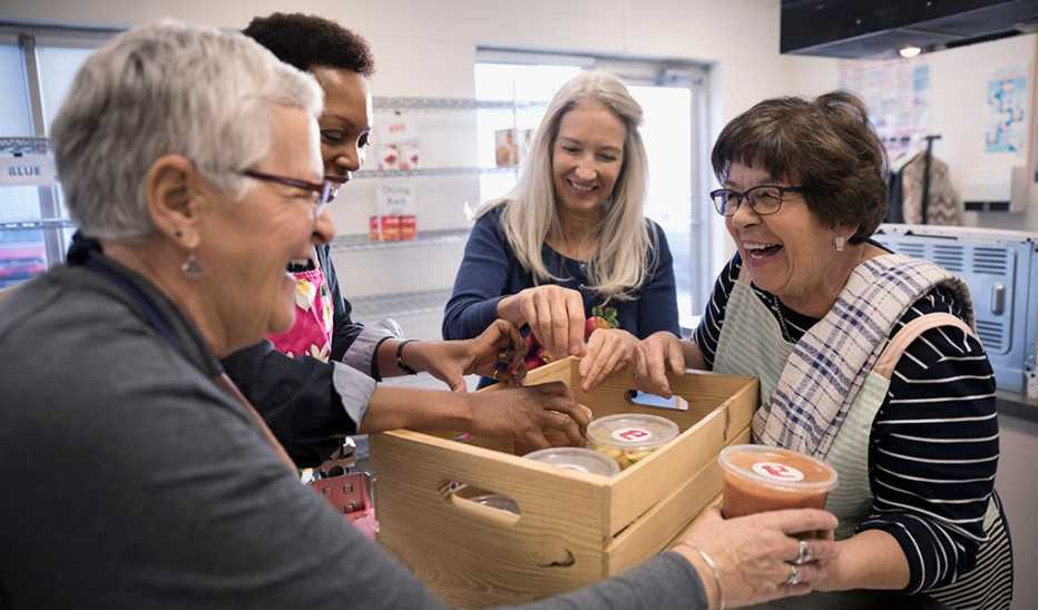 Female volunteers packing soup containers into crate in soup kitchen